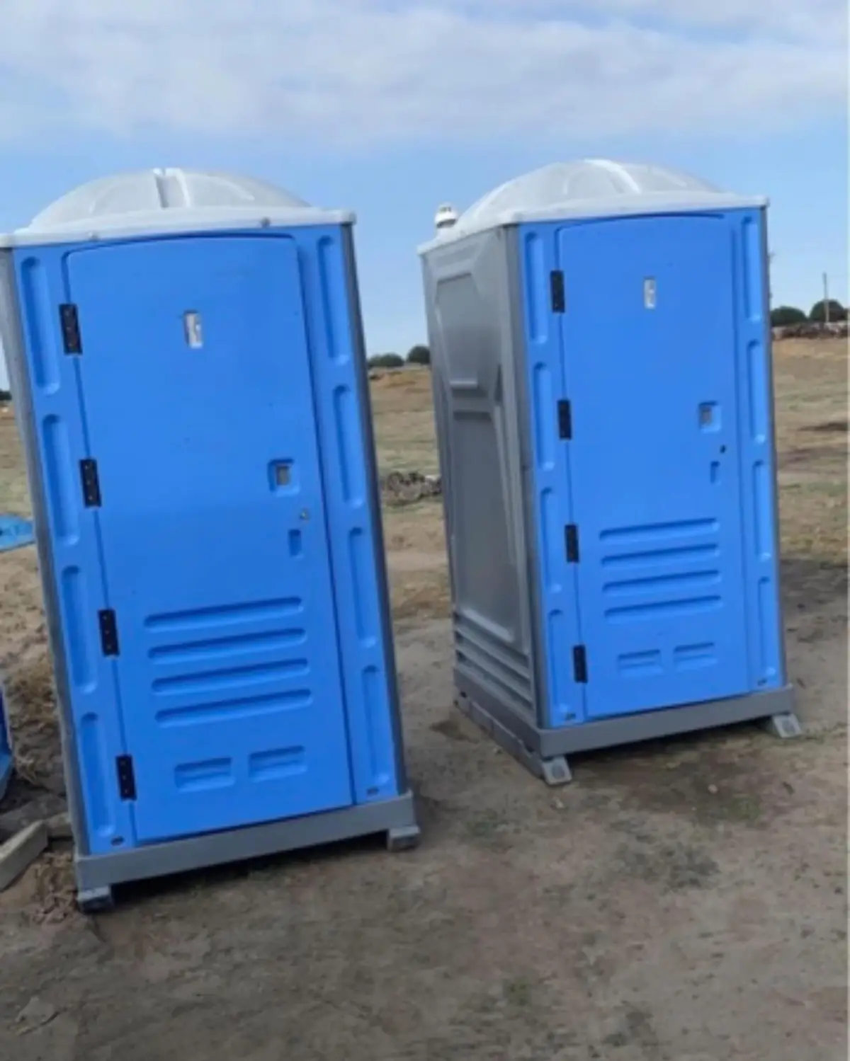 Two standard porta potties on a dirt jobsite lot