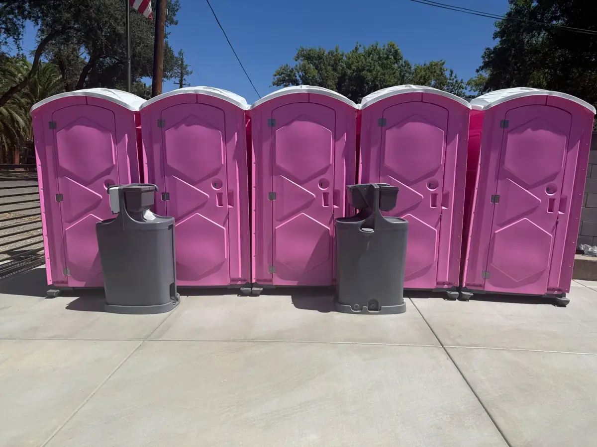 Row of five pink event porta potties with two hand-wash stations on concrete